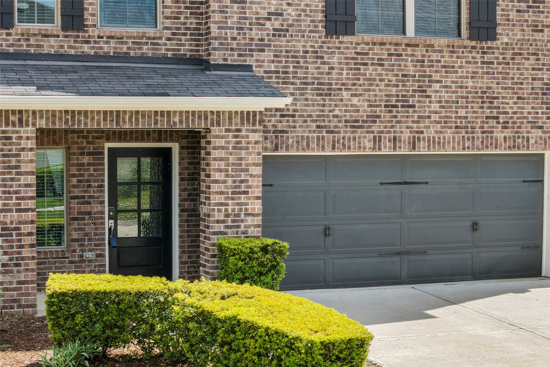 10603 Whitejacket Conroe, TX 77385 - Photo 3 of 42 Brick exterior with a black front door and a two-car garage. The entryway is framed by a neat hedge, enhancing curb appeal.