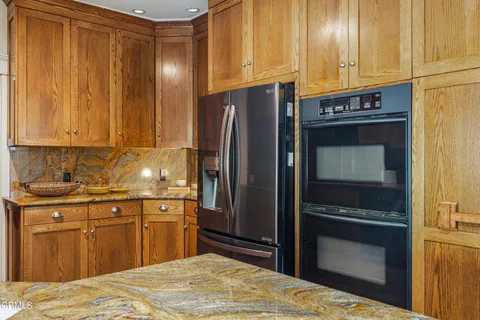 a large kitchen with stainless steel appliances kitchen island granite countertop a refrigerator a oven a dining table and chairs with wooden floor