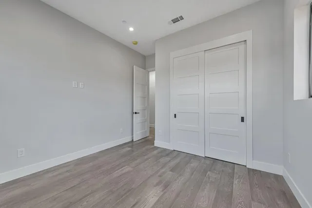 a view of an empty room with wooden floor and closet