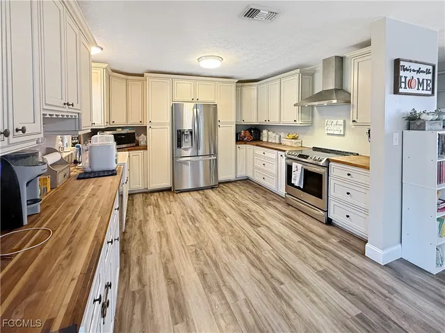 a large kitchen with stainless steel appliances a stove a sink dishwasher a refrigerator white cabinets and wooden floor