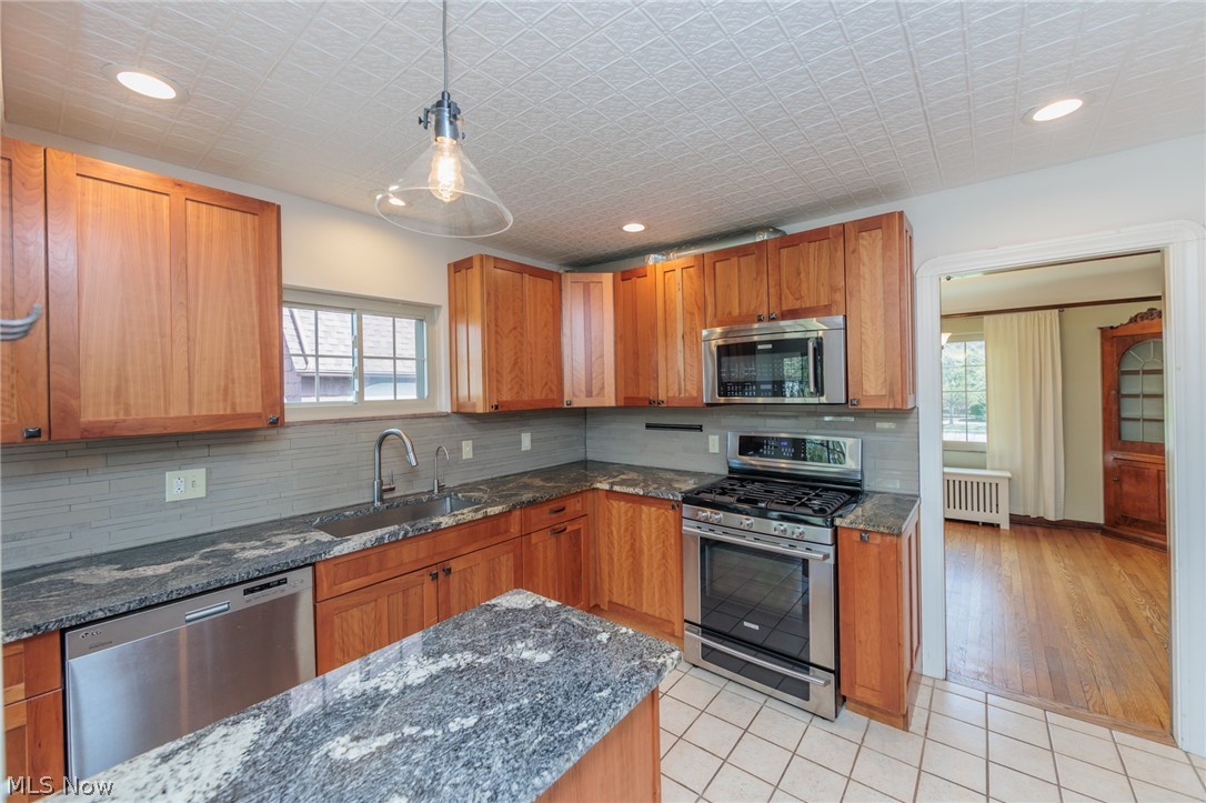 2472 Eaton Road Cleveland, OH 44118 - Photo 15 of 50 Kitchen featuring light tile floors, stainless steel appliances, sink, radiator heating unit, and dark stone counters
