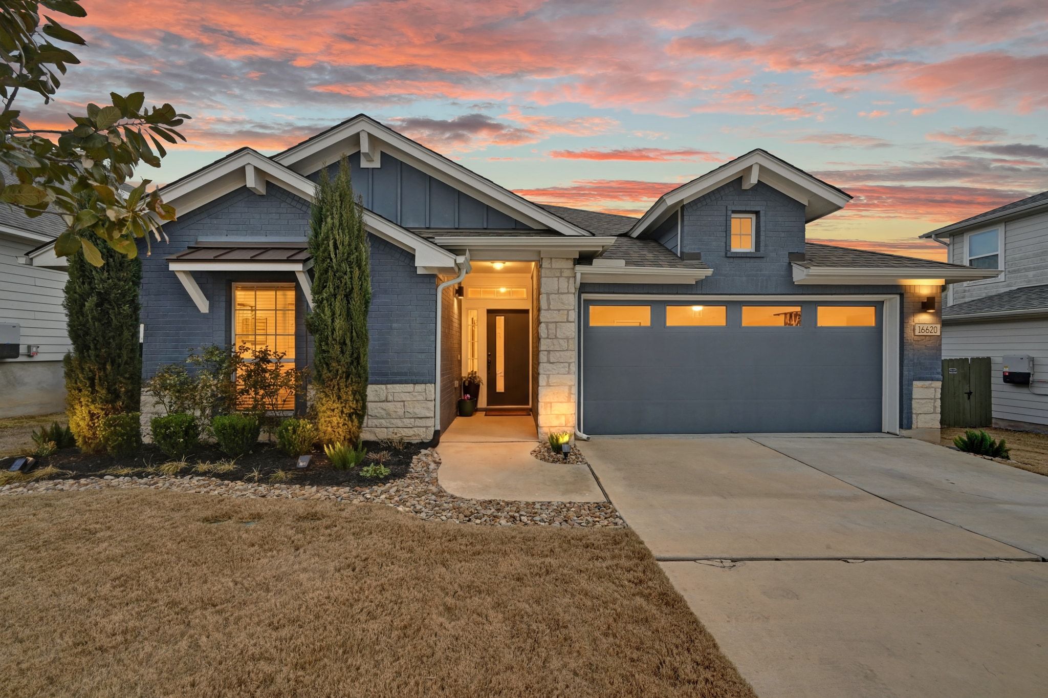 View of front of house with driveway, a yard, board and batten siding, stone siding, 2 car garage