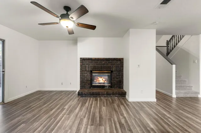 an empty room with wooden floor a ceiling fan and fireplace