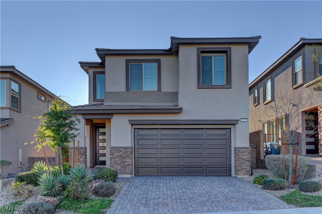 View of front of house with stone siding, stucco siding, a garage, and decorative driveway