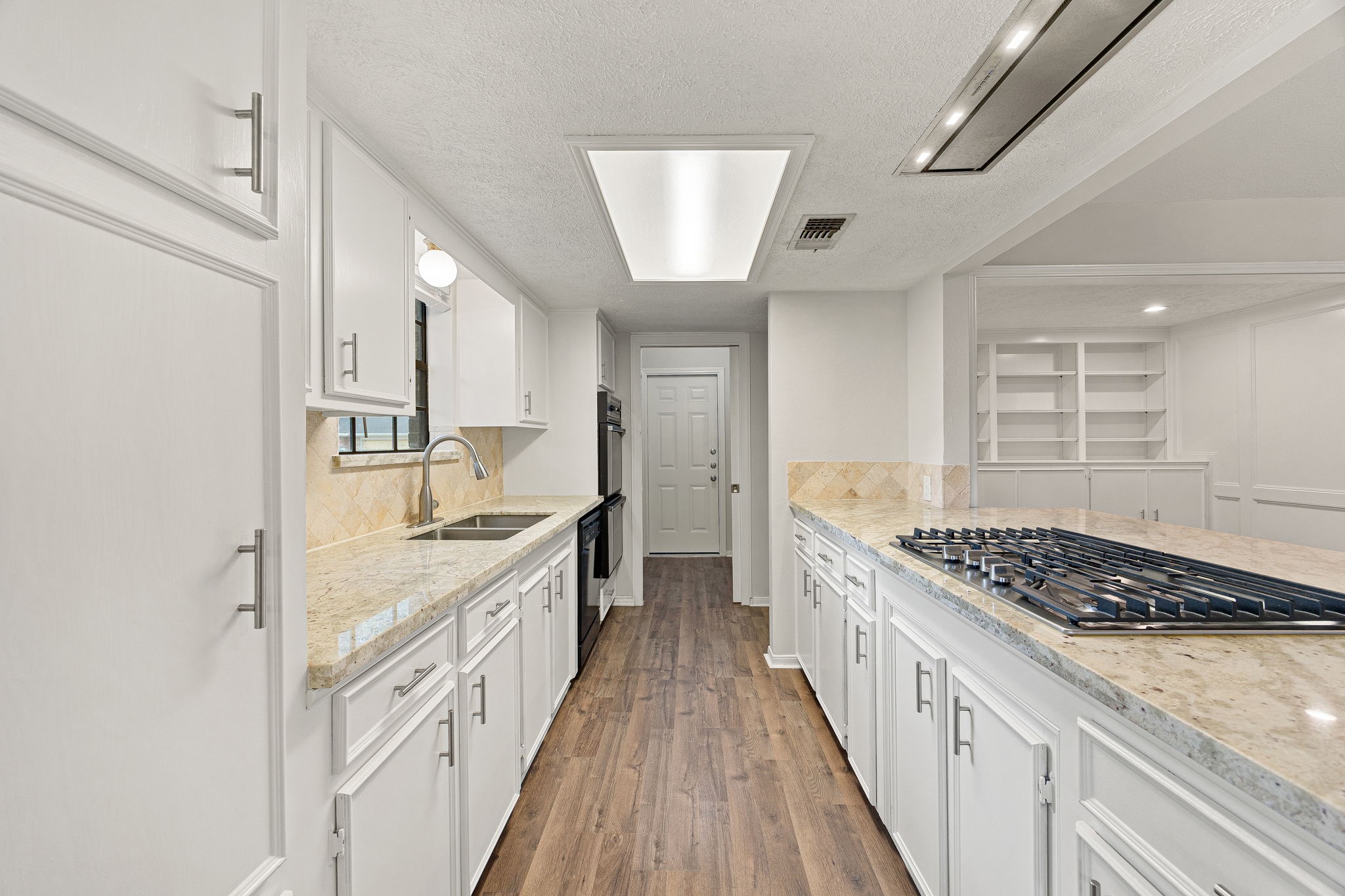 2019 Franklin Circle Rosenberg, TX 77471 - Photo 5 of 19 The renovated kitchen features granite countertops, crisp white cabinetry with brushed-nickel hardware, a travertine tile backsplash, and a stainless double sink beneath a window.