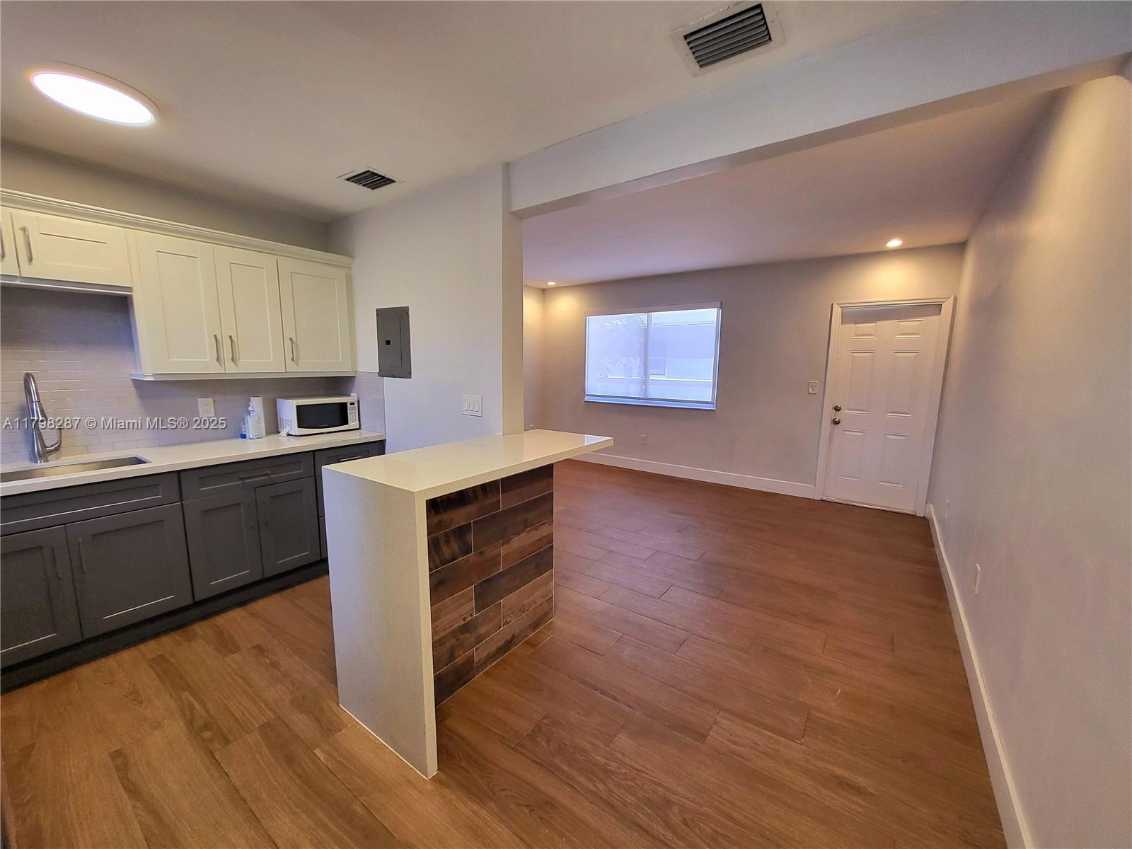 2355 Southwest 27th Street, Unit 4 Miami, FL 33133 - Photo 4 of 25 a kitchen with wooden floors and white cabinets