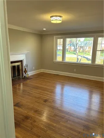 an empty room with wooden floor fireplace and windows