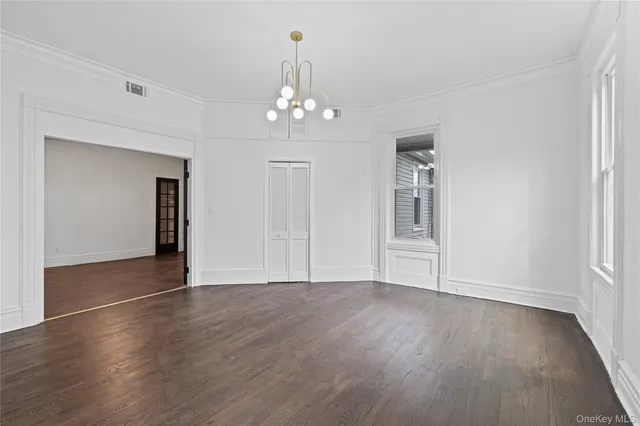 an empty room with wooden floor chandelier and windows