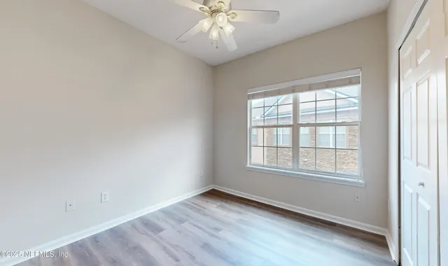 an empty room with wooden floor chandelier fan and windows