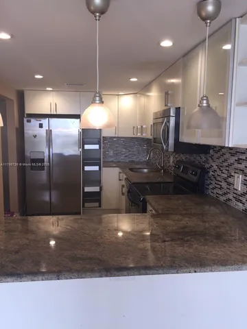 a large kitchen with a large counter top a sink a refrigerator and wooden floor