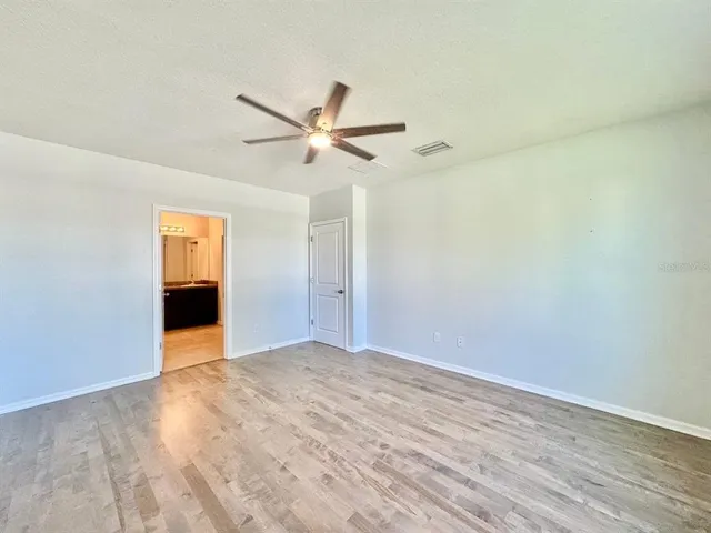 a view of an empty room with wooden floor and a ceiling fan