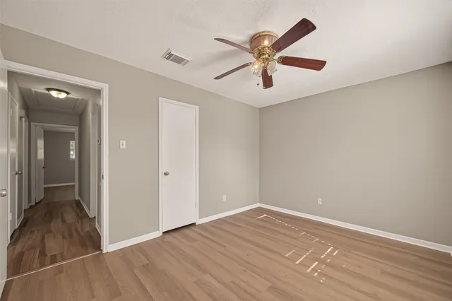 a view of an empty room with wooden floor and a ceiling fan