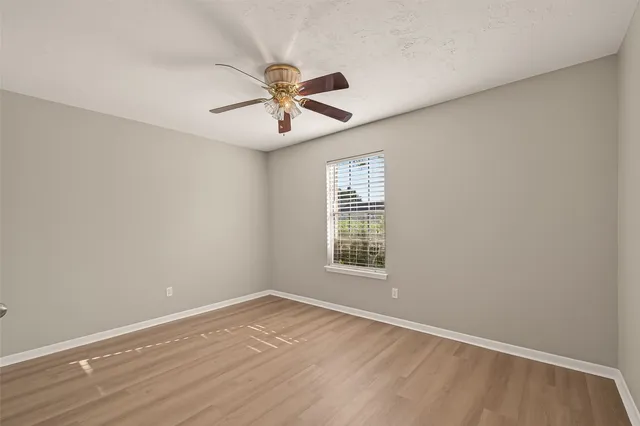 an empty room with wooden floor chandelier fan and windows