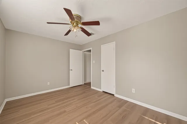 a view of an empty room with wooden floor and a ceiling fan
