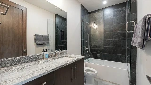 a bathroom with a granite countertop sink a toilet a mirror a bathtub and shower
