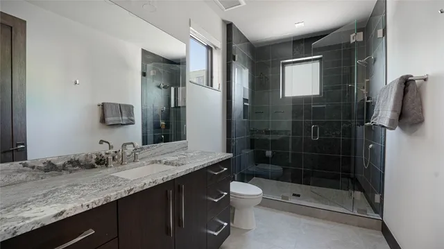 a bathroom with a granite countertop sink a toilet and shower