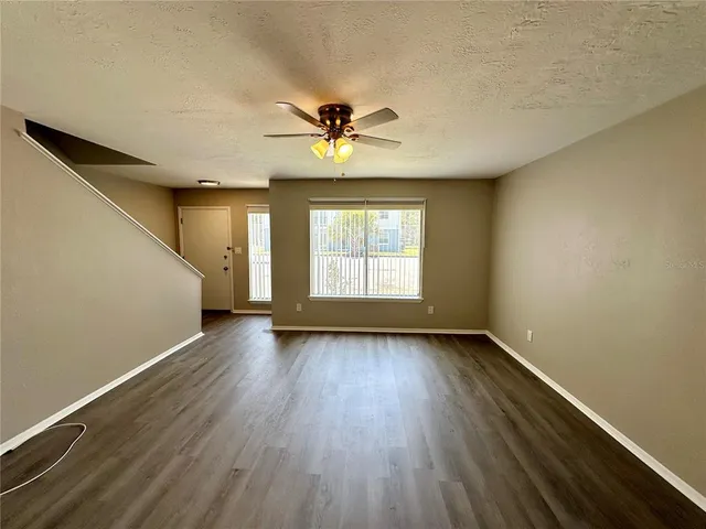 an empty room with wooden floor chandelier fan and windows