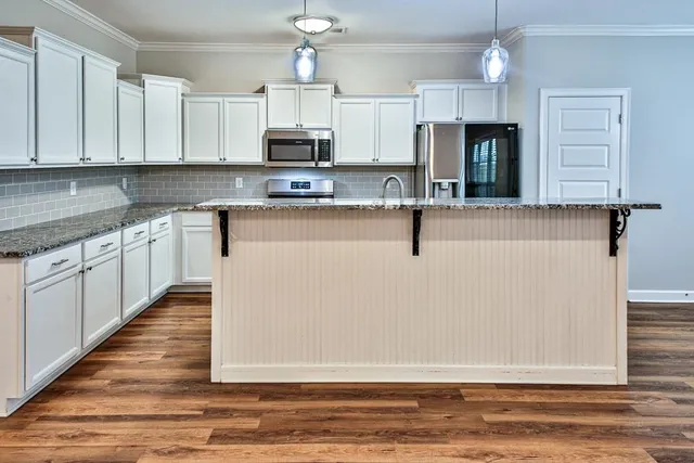 a view of kitchen with stainless steel appliances granite countertop a stove top oven a sink dishwasher and a microwave oven on the wooden floor