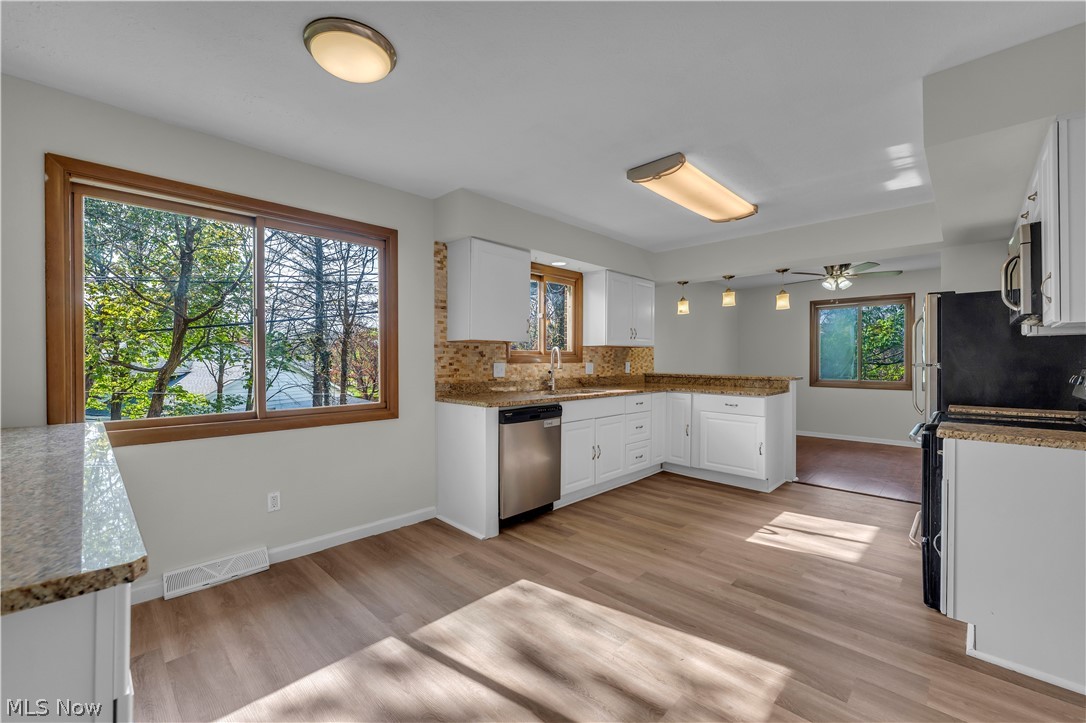 2540 Charney Road University Heights, OH 44118 - Photo 12 of 44 Kitchen featuring wood-finish flooring, white cabinetry, granite countertops with a mosaic tile backsplash, stainless steel appliances, and abundant natural light from multiple windows