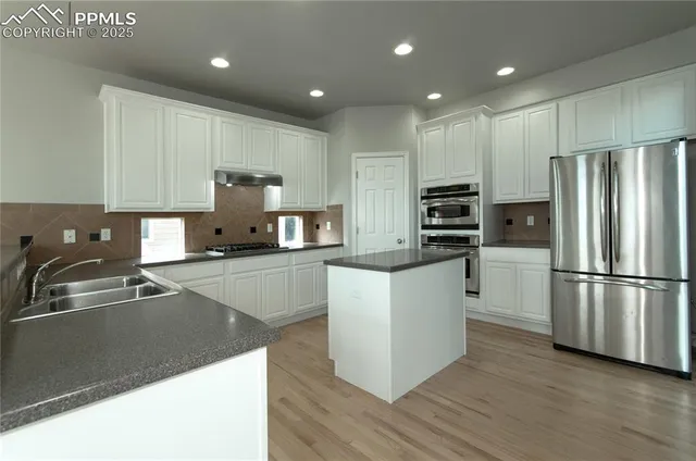 a kitchen with stainless steel appliances granite countertop a refrigerator sink and white cabinets