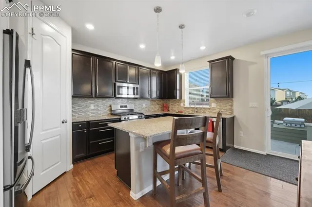 a kitchen with stainless steel appliances granite countertop a stove top oven a refrigerator a sink and chairs