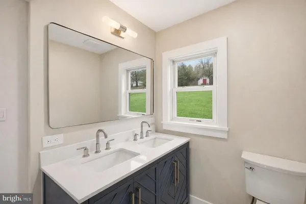 a bathroom with a sink toilet a mirror and next to a window