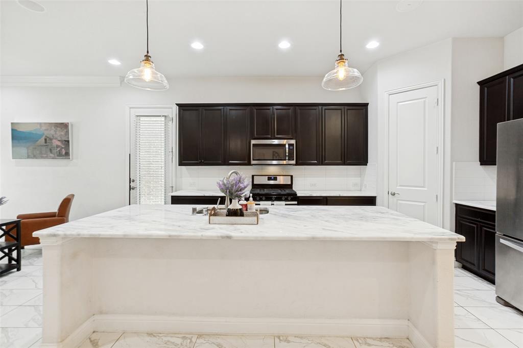 605 Ansley Way Allen, TX 75013 - Photo 15 of 28 Spacious kitchen island featuring a light-toned countertop, clear pendant lighting, dark cabinetry, and integrated stainless steel appliances