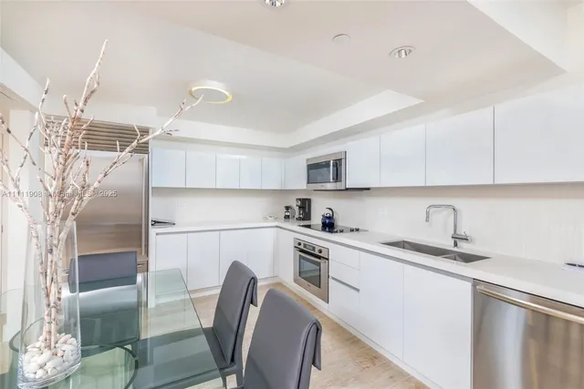 a kitchen with stainless steel appliances granite countertop a sink a stove a refrigerator with white cabinets and wooden floor