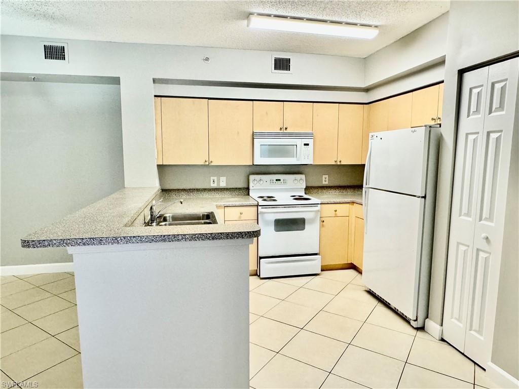 1200 Reserve Way, Unit 103 Naples, FL 34105 - Photo 6 of 26 a kitchen with granite countertop a refrigerator a stove a sink a washer and dryer