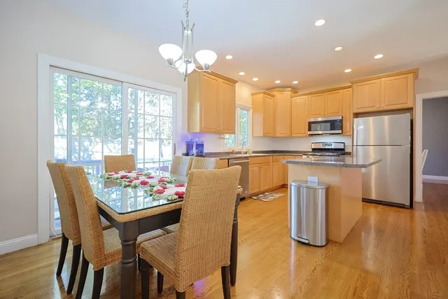 a kitchen with stainless steel appliances granite countertop a stove a refrigerator a microwave a dining table and chairs with wooden floor