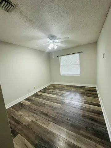 an empty room with wooden floor fan and windows