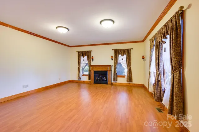 a view of an empty room with wooden floor fireplace and a window