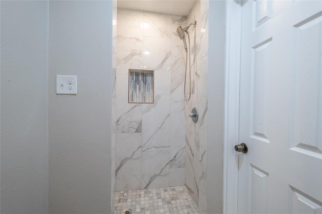 11005 Ferguson Road Dallas, TX 75228 - Photo 18 of 23 Walk-in shower with large-format tile walls, mosaic tile flooring, a built-in shower niche, and a brushed nickel shower head