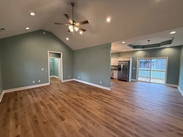 a view of an empty room with wooden floor and a kitchen
