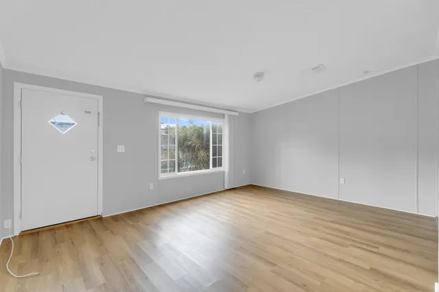 a view of an empty room with wooden floor and a window