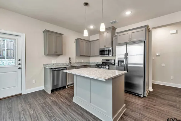 a kitchen with stainless steel appliances granite countertop a refrigerator a sink dishwasher a stove and white cabinets with wooden floor