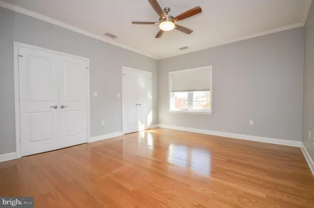 an empty room with wooden floor fan and windows