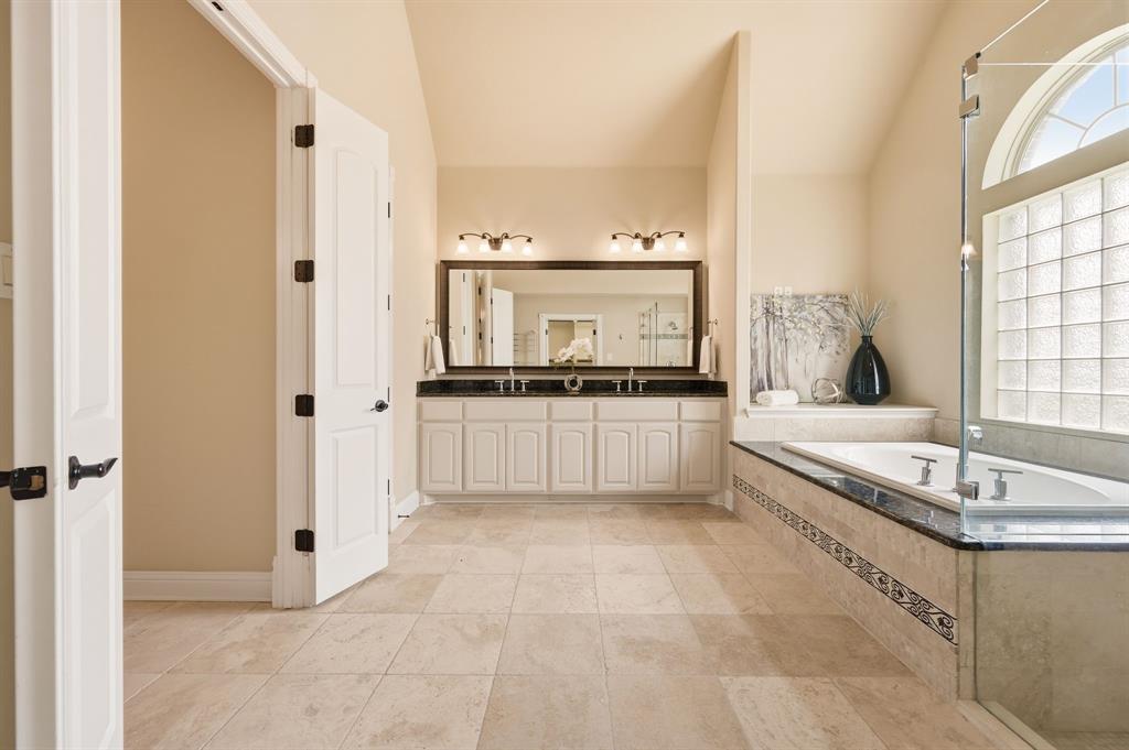 7013 Handel Colleyville, TX 76034 - Photo 21 of 37 Spacious bathroom featuring a dual vanity with a dark countertop, an integrated bathtub with a tiled surround, a glass block window, and light-toned tile flooring