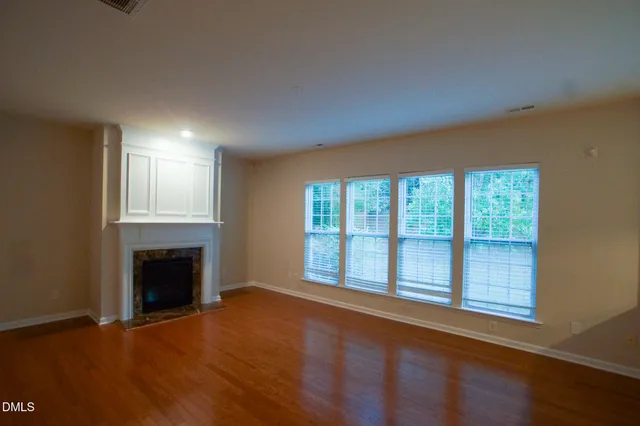 an empty room with wooden floor fireplace and windows