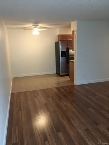 a view of empty room with wooden floor and kitchen