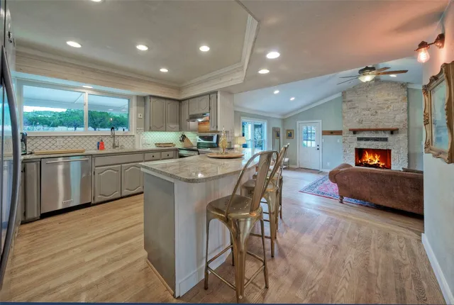 a kitchen with stainless steel appliances granite countertop wooden cabinets a sink dishwasher a stove and a refrigerator with wooden floor