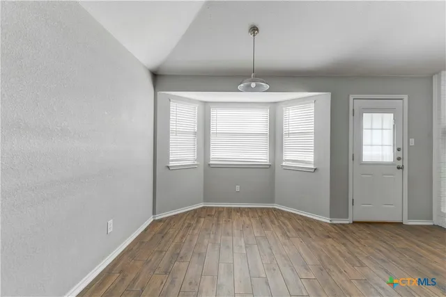 a view of an empty room with window and wooden floor