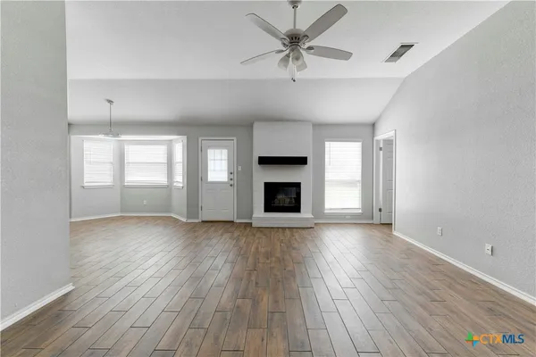 an empty room with wooden floor fireplace and windows