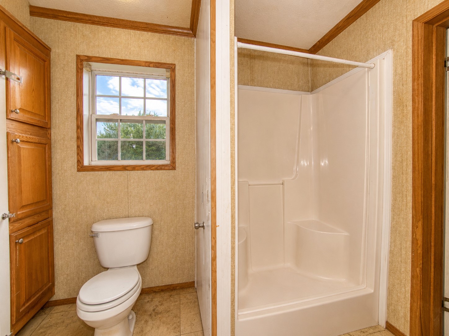 461924 East 1140 Road Sallisaw, OK 74955 - Photo 18 of 29 Bathroom featuring a white toilet, built-in shower, wood-finish cabinetry, and a window with wood-finish trim