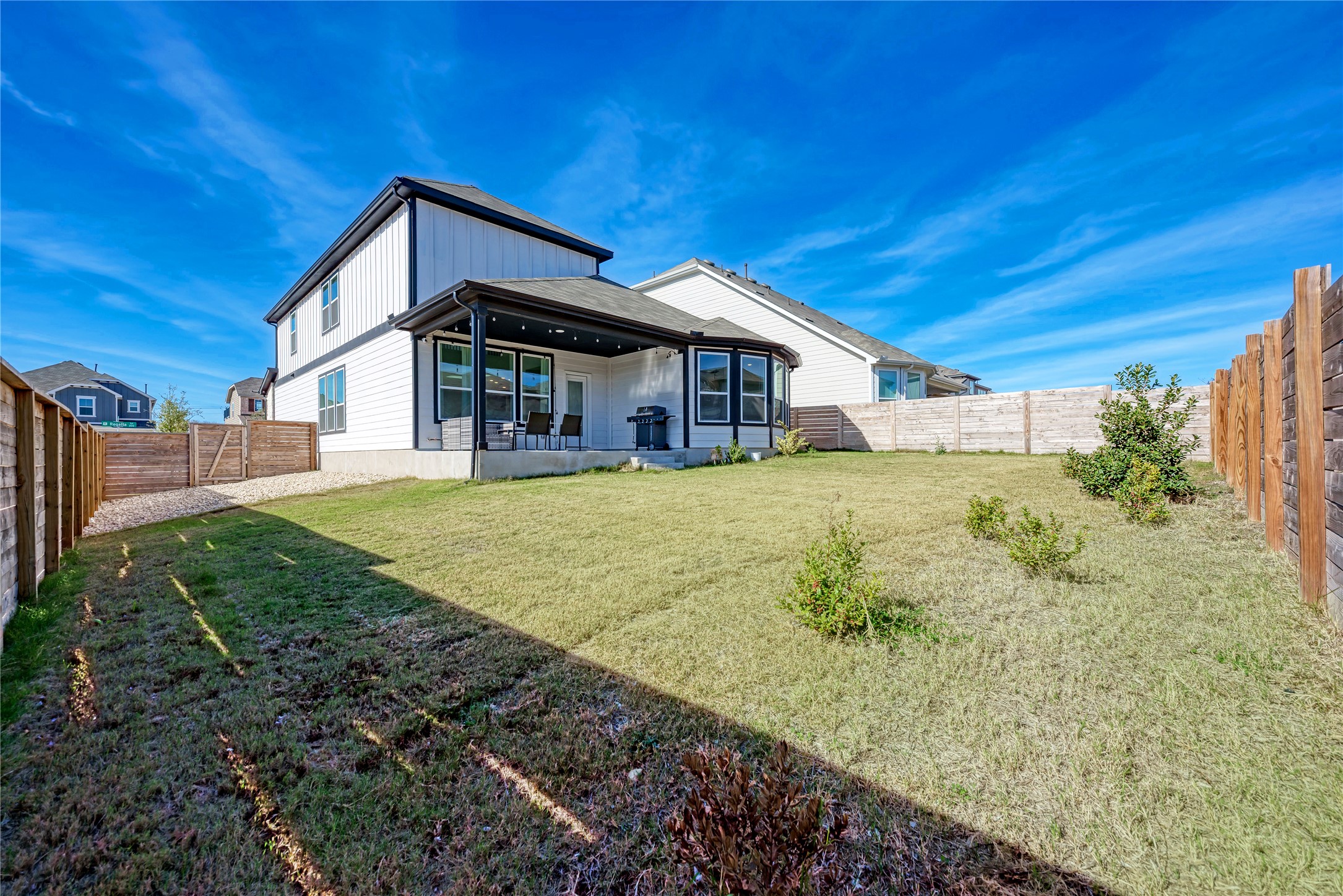 316 Regatta Trail Leander, TX 78641 - Photo 34 of 39 Expansive fenced backyard featuring a covered patio, a two-story home exterior with white siding and dark trim, a manicured lawn, and a gravel side yard with a wooden gate