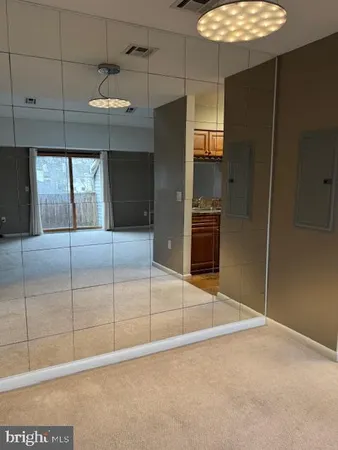 an empty room with chandelier fan and kitchen view