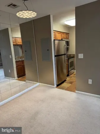 a view of a refrigerator in kitchen and an empty room with wooden floor