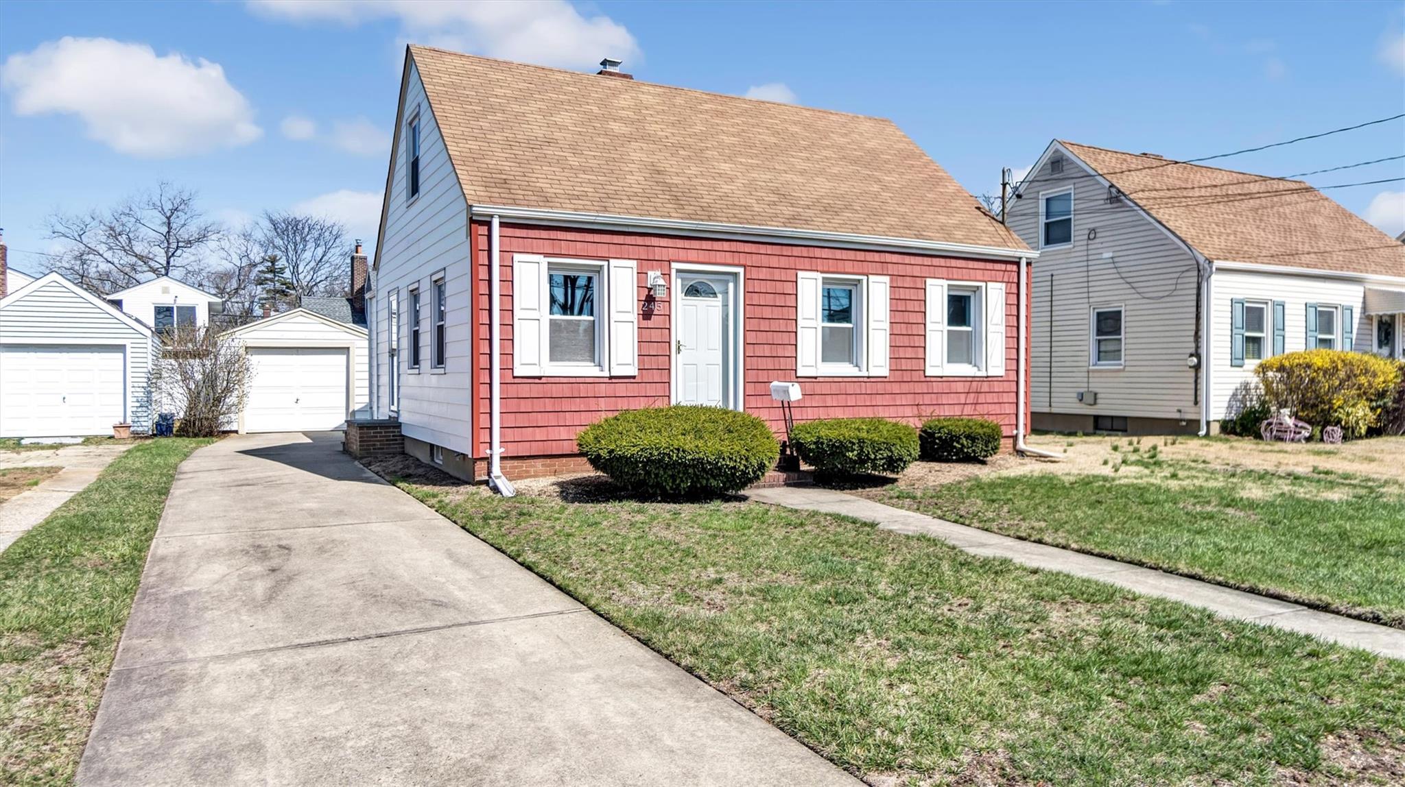 View of front of house with a front yard, a detached garage, an outdoor structure, and a shingled roof