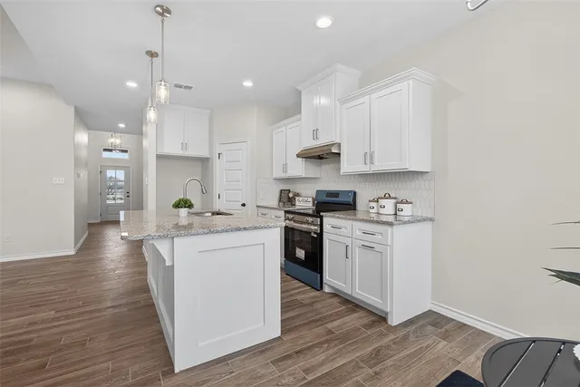 a kitchen with stainless steel appliances granite countertop a stove top oven a sink a refrigerator and white cabinets with wooden floor