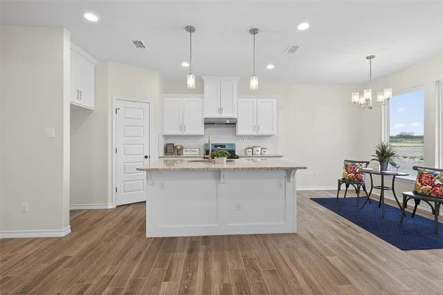 a kitchen with stainless steel appliances granite countertop a stove a sink a refrigerator and a dining table with wooden floor